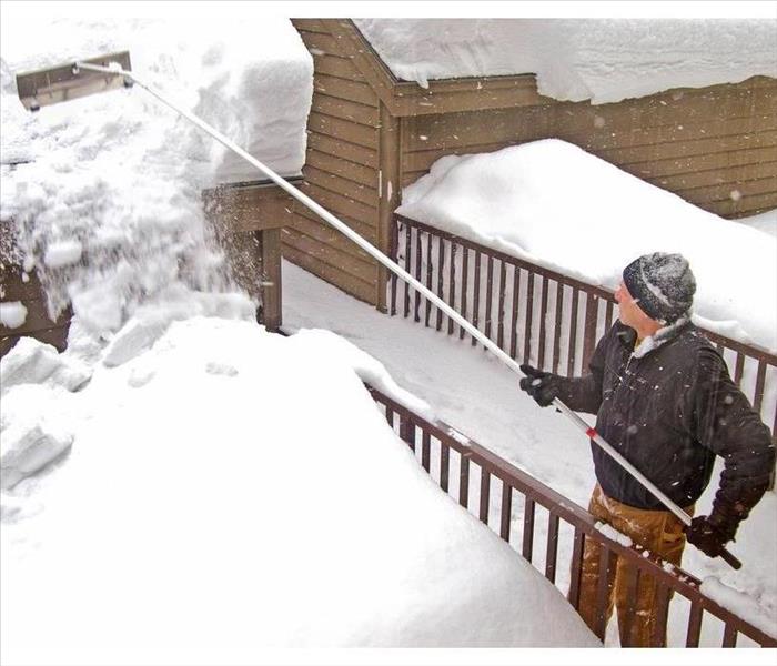 man using a snow rake on garage roof in winter