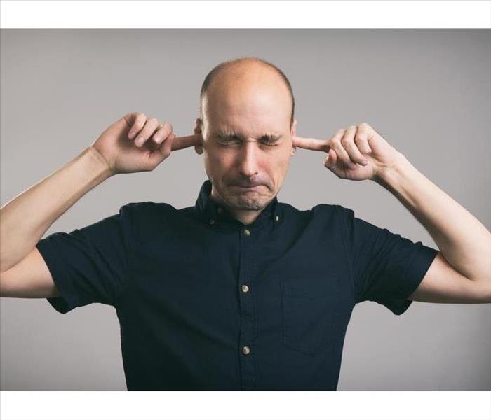 bald man covering his ears over gray background